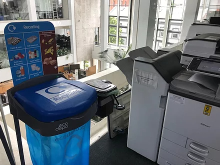 blue recycling bin for paper recycling in an office - placed beside a photocopier
